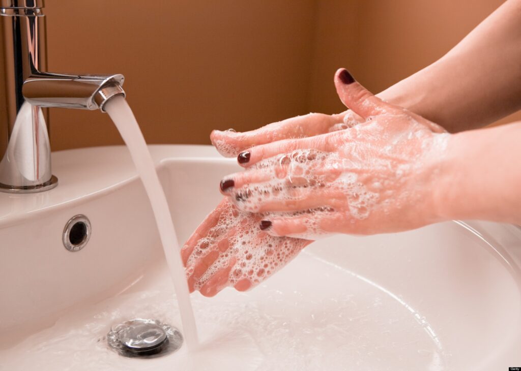 Picture showing bubbly hands performing hand washing under a running faucet.